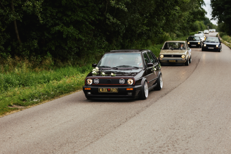 Sportowy Volkswagen udekorowany ślubnie jedzie drogą.