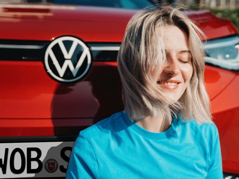 Eine zufriedene Frau sitzt vor einem roten VW ID.4 GTX.