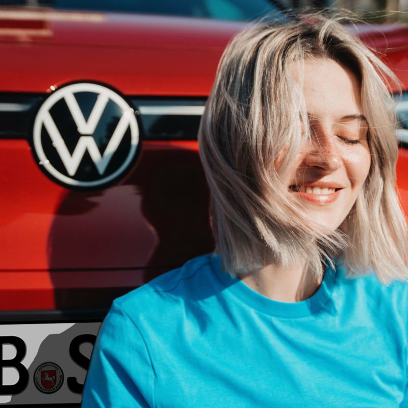 Eine zufriedene Frau sitzt vor einem roten VW ID.4 GTX.