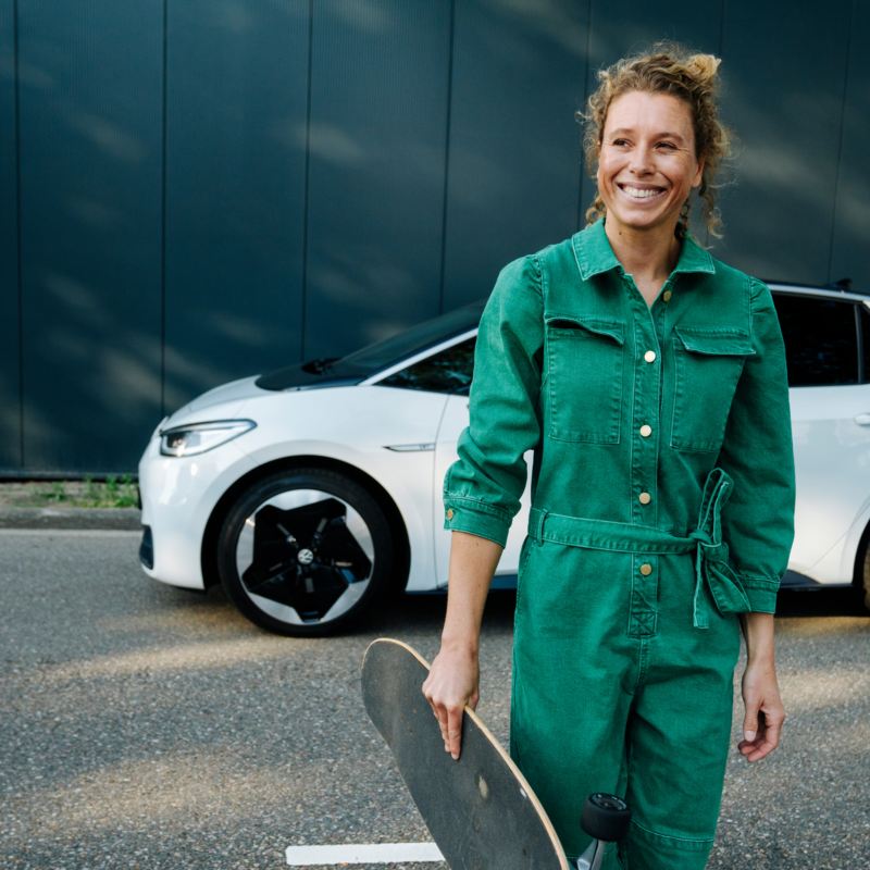 Frau mit Skateboard vor einem weißen VW ID.3 Modell.