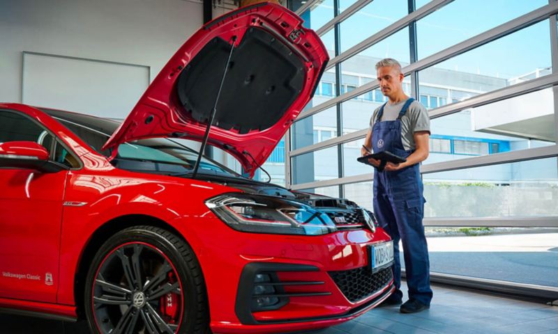 Golf GTI rouge avec le capot ouvert. Un technicien inspecte le véhicule.