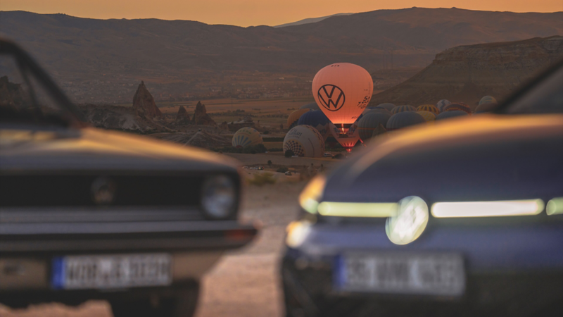 2 Golf Modelle stehen auf einem Platz, während ein Heissluftballon im Hintergrund landet