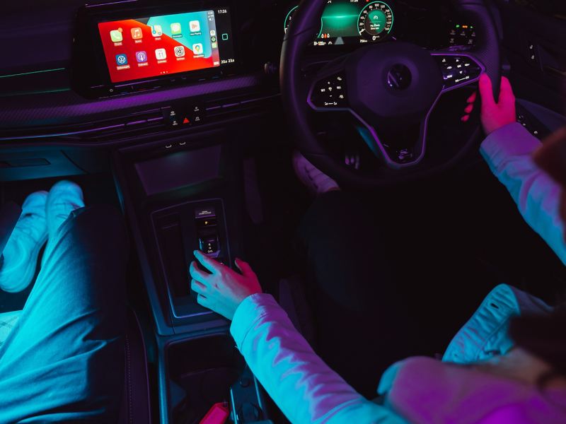 Wide image of Volkswagen Golf interior in the dark, lit by neon lights and ambient lighting.