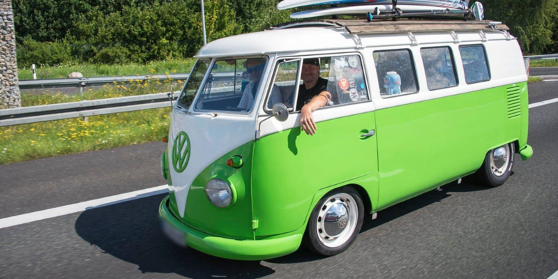 Et gammelt folkevognsrugbrød i farverne grøn og hvid med et surfbræt på taget.