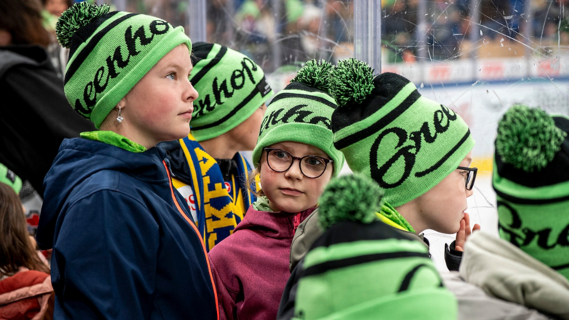 Un gruppo di bambini con cappelli verdi con la scritta «Greenhope» guarda con interesse il campo di gioco di una pista di pattinaggio.