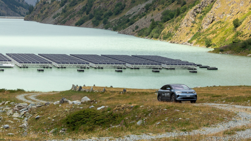 L'ID.5 GTX roule sur un chemin de terre et on peut voir en arrière-plan les panneaux solaires sur le lac des Toules.