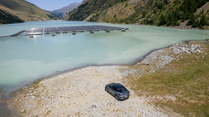 L'ID.5 GTX roule sur un chemin de terre et on peut voir en arrière-plan les panneaux solaires sur le lac des Toules.