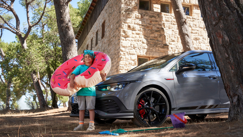 Et barn står med en badering og svømmebriller foran en Golf GTI