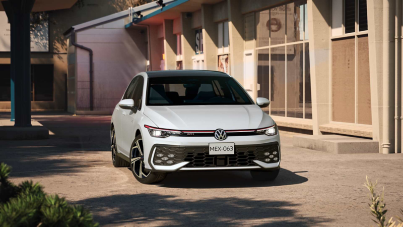 Golf GTI en color blanco transita cerca de un conjunto de edificios comerciales.