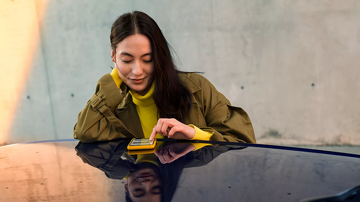 Person leant against car scrolling phone that's resting on the car roof