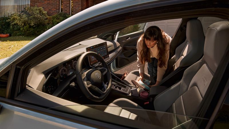 Eine Frau lehnt sich in einen VW und greift nach Kopfhörern, welche auf dem Beifahrersitz liegen.