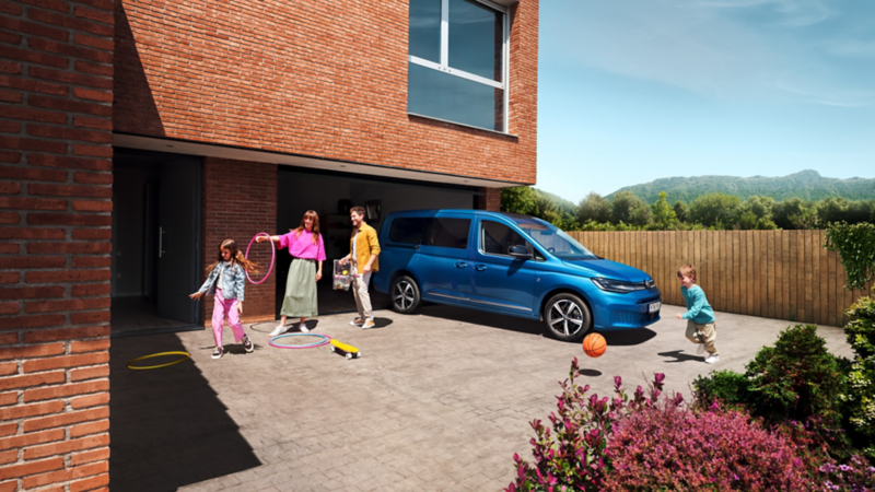 Une famille joue dans l'allée, à côté du Volkswagen Caddy.