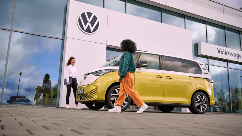 Una mujer del servicio técnico de VW hablando con una mujer, al lado del VW ID. Buzz.
