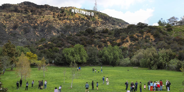 Menschen stehen auf einer grünen Wiese, im Hintergrund der Schriftzug des Hollywood Sign.