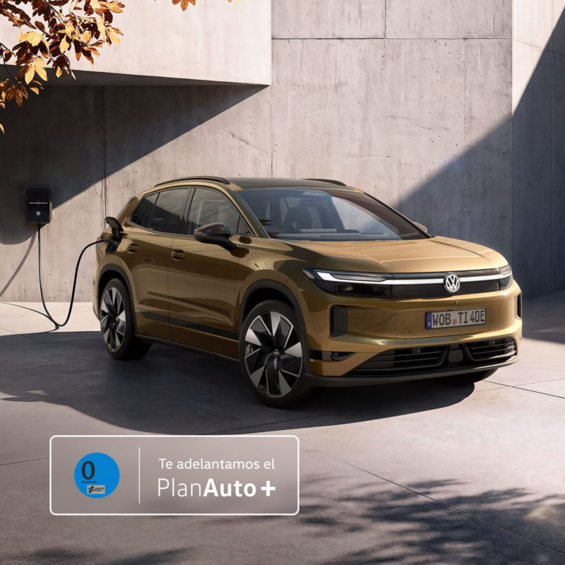 Un VW ID. Tiguan de color bronce oliva está aparcado junto a un punto de carga mural frente a una casa moderna con el logo de Plan Auto+