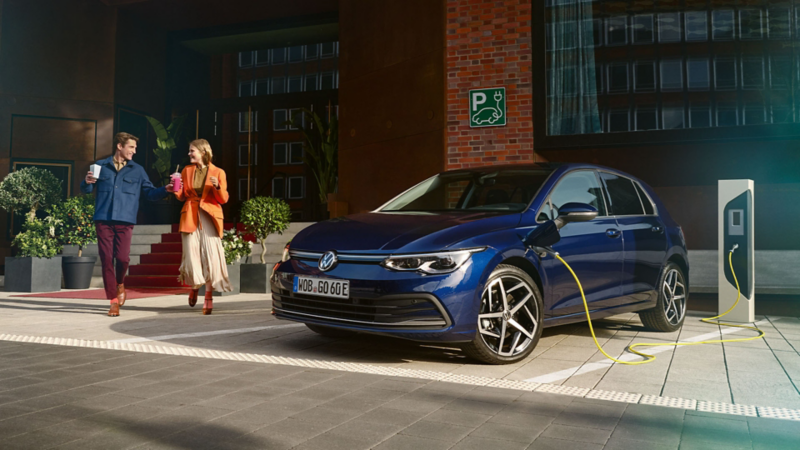 A couple walking past a VW PHEV that is being charged from a public charging station