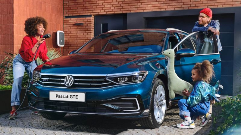 A woman holding a charging cable next to a VW Passat GTE with a father and daughter onlooking