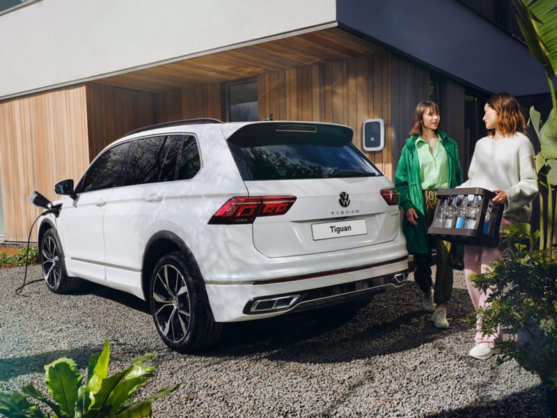 Two people standing by the rear of a white Tiguan eHybrid that is plugged in to a charger