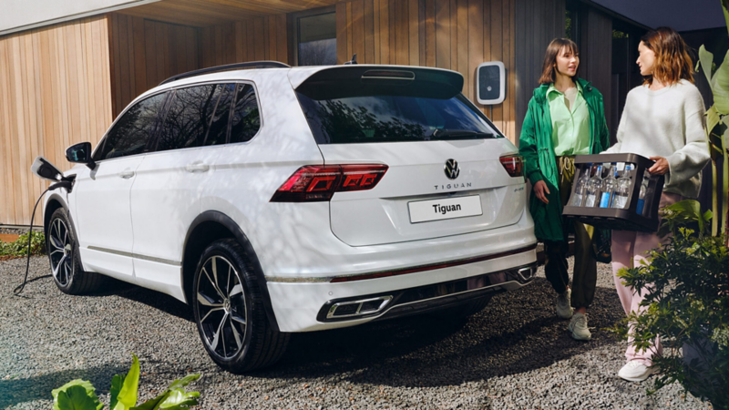 the back of a Tiguan plugged in charging with a couple standing next to it 