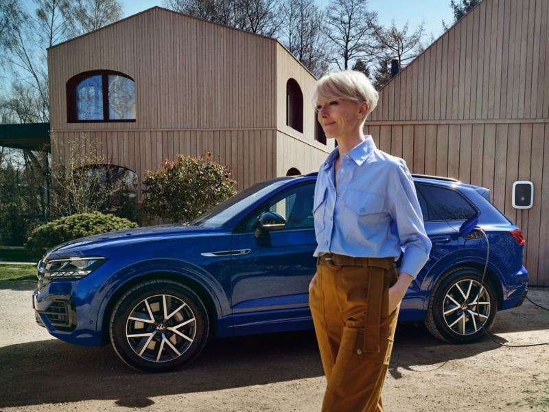 A woman stands in front of a charging VW Touareg R eHybrid.