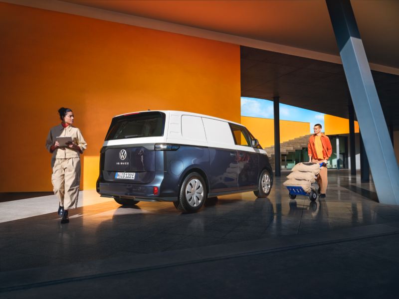 Kobieta i mężczyzna wkładają załadunek do biało-niebieskiego ID. Buzz Cargo, elektrycznego samochodu dostawczego Volkswagena.