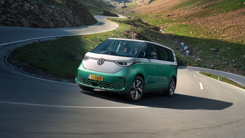  Un Volkswagen ID. Buzz bicolore, vert menthe et blanc, roule sur une route sinueuse de montagne.