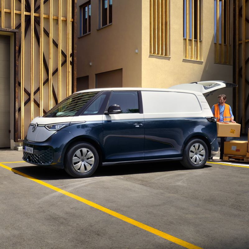 Un VW ID. Buzz Cargo bleu et blanc devant un hangar se faisant charger par 1 personne