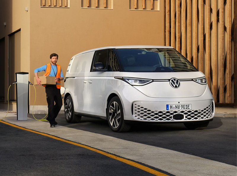 Volkswagen ID. Buzz Cargo parked at a charging point while a delivery worker carries a parcel.