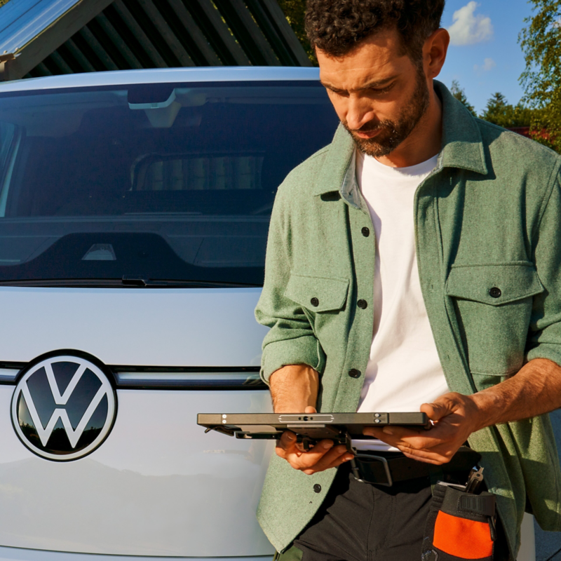 Ein Handwerker lehnt an einem ID. Buzz Cargo und schaut auf sein Tablet.