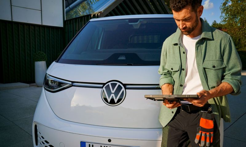 Ein Handwerker steht neben einem VW ID. Buzz Cargo und blickt auf ein Tablet.