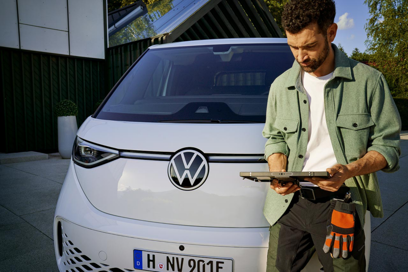 Mężczyźni w pomarańczowych kamizelkach odblaskowych patrzą na dokumenty rozłożone na masce dostawczego Volkswagena.