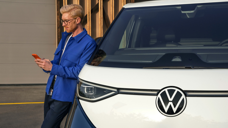 Un hombre apoyado en un VW ID. Buzz, mirando un móvil.