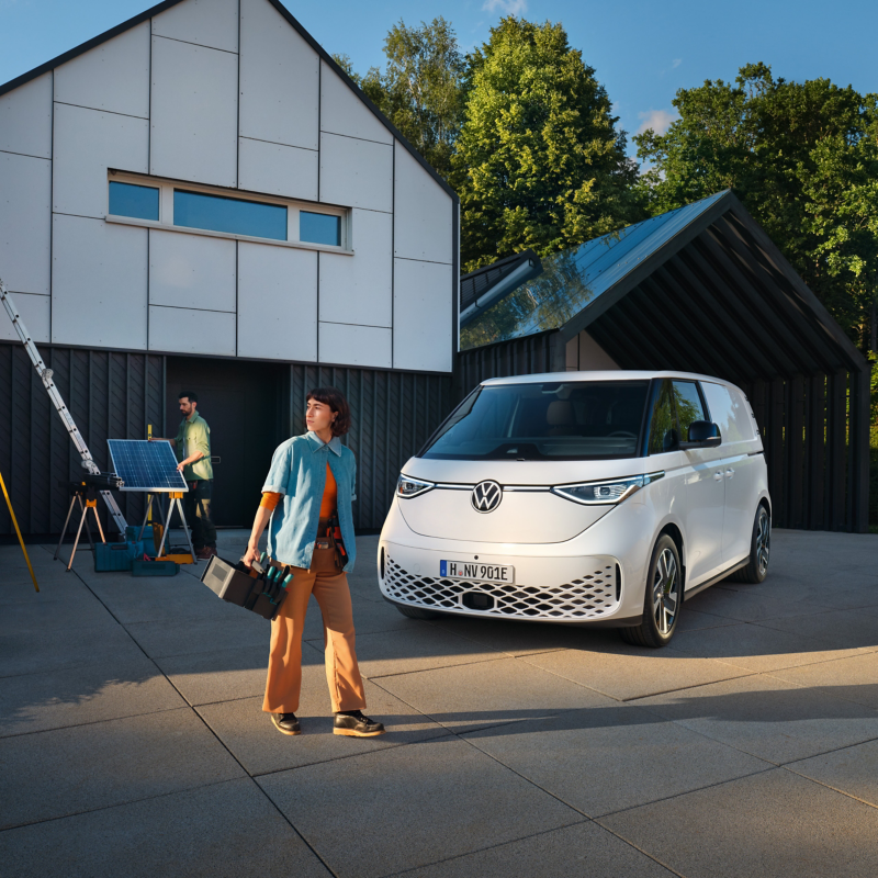 Eine Handwerkerin mit Werkzeugkasten in der Hand steht vor einem geparkten VW ID. Buzz Cargo.