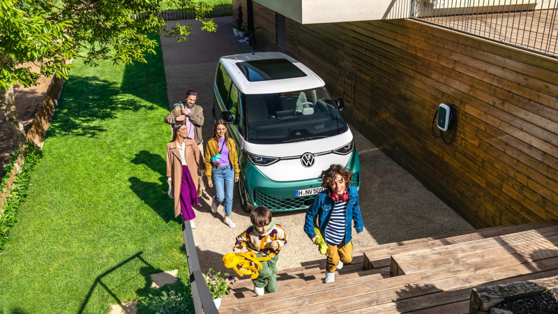 En familj samlad runt en VW ID Buzz på laddning vid en wallbox.