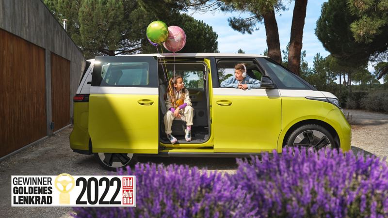 Zwei Kinder mit Luftballons sitzen im parkenden VW ID. Buzz.