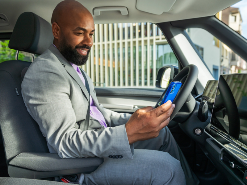 Ein Mann im Anzug sitzt in einem VW ID. Buzz und blickt auf sein Smartphone.