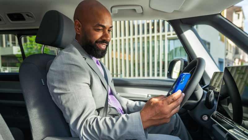 Ein Fahrer sitzt in einem VW ID. Buzz und blickt auf sein Handy.