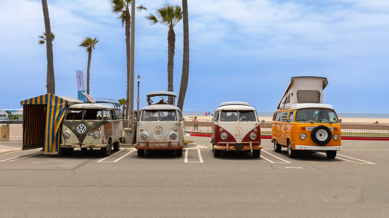 Quattro storici Volkswagen Bulli parcheggiati di fronte ad una spiaggia.