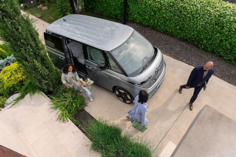 Top down Ansicht auf einen VW ID. Buzz, welcher in einer Einfahrt parkt und eine Familie aussteigt.