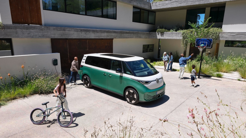 Un hombre del servicio técnico de VW sujetando el conector de carga con un VW ID. Buzz detrás.