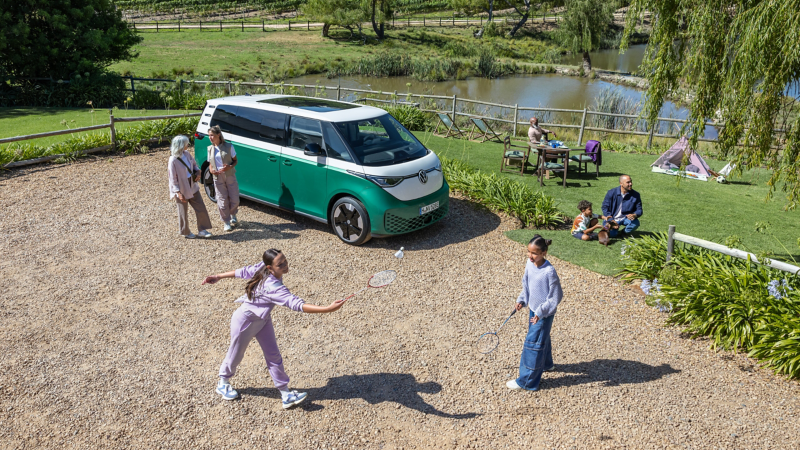 Familie spielt im Park, daneben parkt ein VW ID. Buzz.