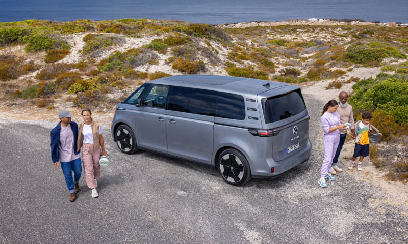 VW ID. Buzz parkt in den Dünen am Meer. Um ihn herum eine Familie mit Kindern.
