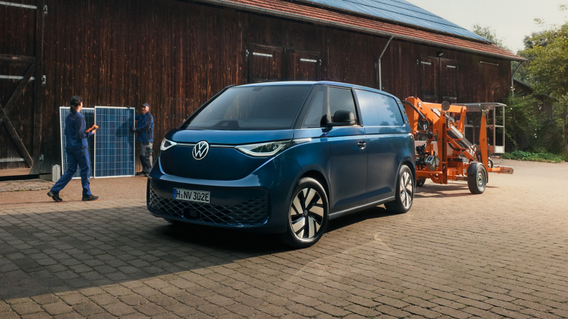 VW ID. Buzz Cargo Pro parkt neben einer Scheune mit Solardach.