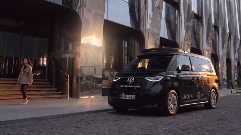 Autonomously driven ID. Buzz is parked in front of a modern building.