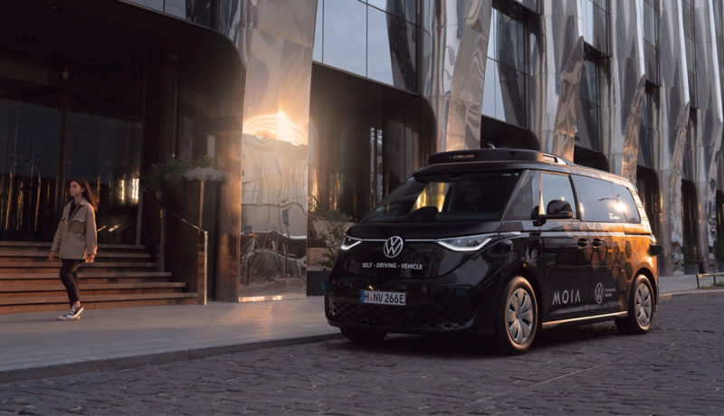 Selbstfahrender VW ID. Buzz von MOIA parkt vor einem modernen Gebäude.