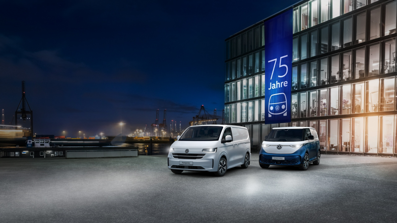 Ein VW Transporter Kastenwagen und ID. Buzz Cargo stehen bei Nacht vor einem Bürogebäude im Hafen.
