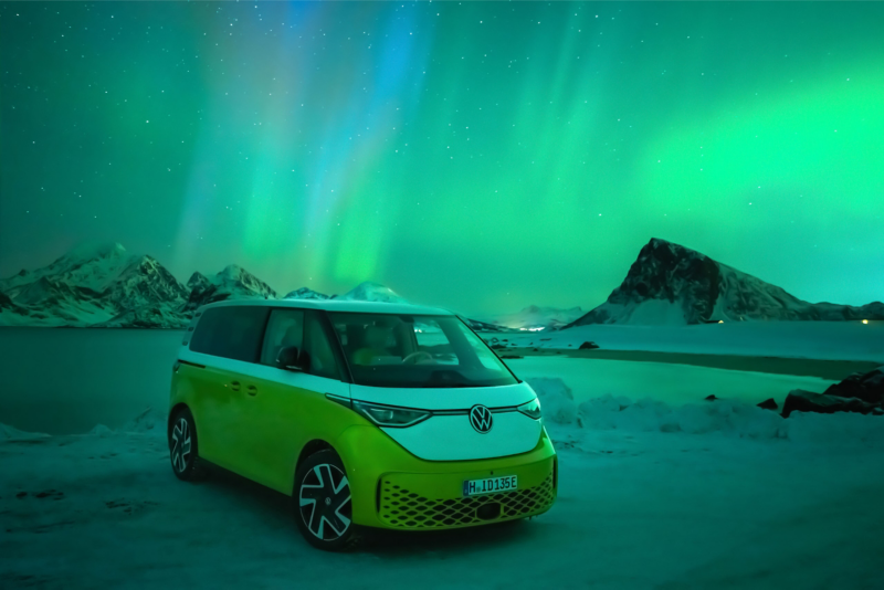 Der VW ID. Buzz steht in einer verschneiten Landschaft bei Dämmerung, am Himmel sieht man Polarlichter.