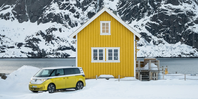 Der VW ID. Buzz steht vor einem kleinen, gelben Haus in einer verschneiten Landschaft.