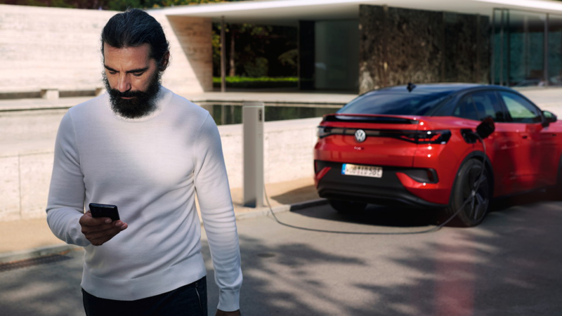Ein Mann mit Smartphone geht an einem roten VW ID.5 GTX vorbei, der an einer Ladestation lädt.