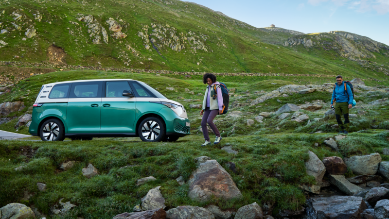 Una mujer y un hombre bajando una colina con el VW ID. Buzz aparcado al lado.